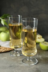 Glasses of delicious cider and green apples on gray table, closeup