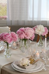 Stylish table setting with beautiful peonies and burning candles indoors