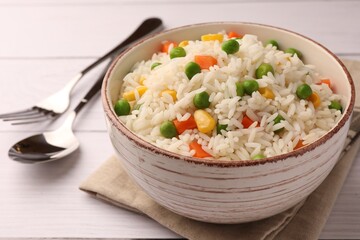 Bowl of delicious rice with vegetables served on white wooden table, closeup