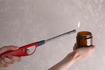 Woman lighting candle with gas lighter against grey wall, closeup