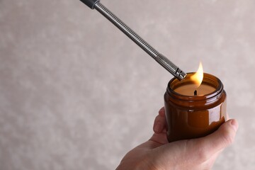 Woman lighting candle with gas lighter against grey wall, closeup
