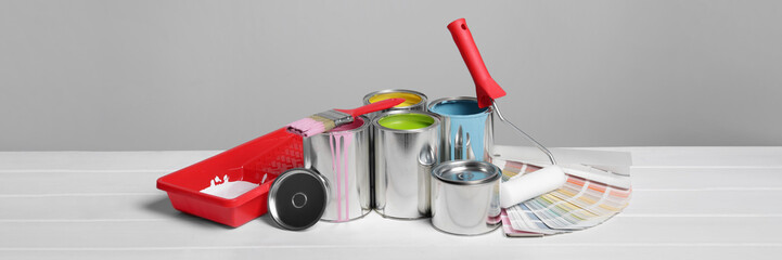 Cans of paints, roller, tray and palette on white wooden table. Banner design