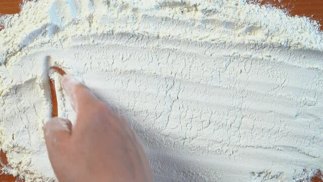 Finger uncertainly writes word supper on white flour scattered on table, confidently underlines letters. Advertising screensaver for culinary master class for beginners baking recipes, culinary rules