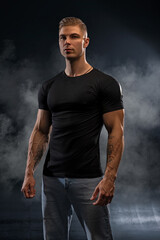 Athletic sexy man in black t-shirt and jeans posing in studio