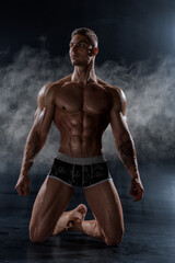Obraz na płótnie Canvas Muscular shirtless man with perfect body posing kneeling in studio