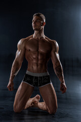 Fototapeta na wymiar Muscular shirtless man with perfect body posing kneeling in studio