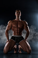 Obraz na płótnie Canvas Muscular shirtless man with perfect body posing kneeling in studio