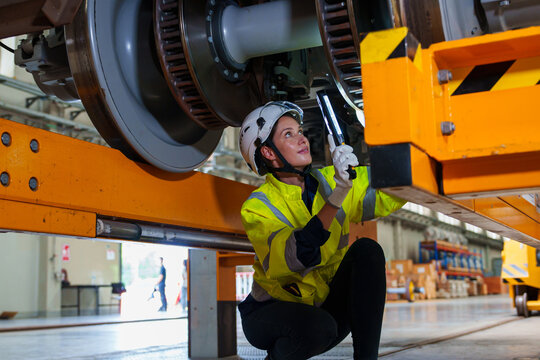 Railway technician engineer woman holds a light stick to check and fix the problem under an electric train for working at a sky train or depot maintenance plant.
