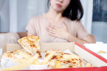 Asian woman having chest and stomach pain after overeating pizza, heartburn from acid reflux   caused by GERD