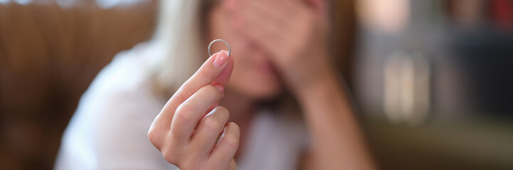 Woman holds wedding ring in hands and cries at home