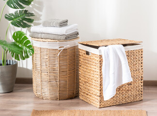 Two natural wicker laundry baskets filled with white towels, set on a wooden floor in a cozy room...