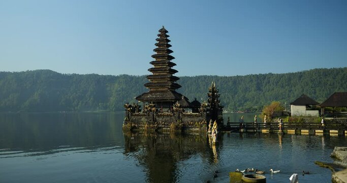 Slow motion panning shot of Pura Ulun Danu temple with view of volcanic lake and surrounding nature with swimming ducks