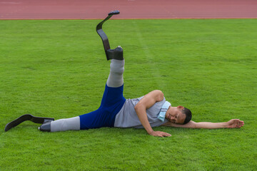 Asian athlete with prosthetics stretches on grass lawn, concluding his speed running practice at the stadium