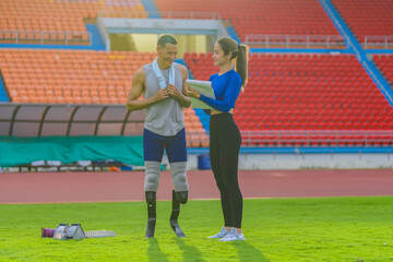 Male athlete with prosthetic blades, alongside female trainer, outlining the day's speed running training at the sports stadium