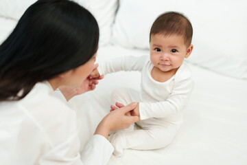 happy mother and infant baby sitting and playing on a bed