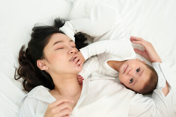 happy mother lying and playing with her infant baby on bed (top view)