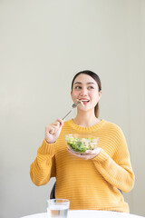 Happy young Asian woman with fresh vegetables and fresh fruits, healthy concept working lunch at home, beautiful woman with laptop eating salad, lifestyle in living room concept.