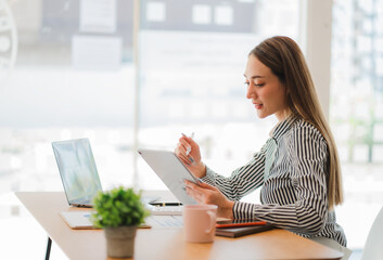 Asian businesswoman in suit sitting on desk in office, with computer document graph for bookkeeping...