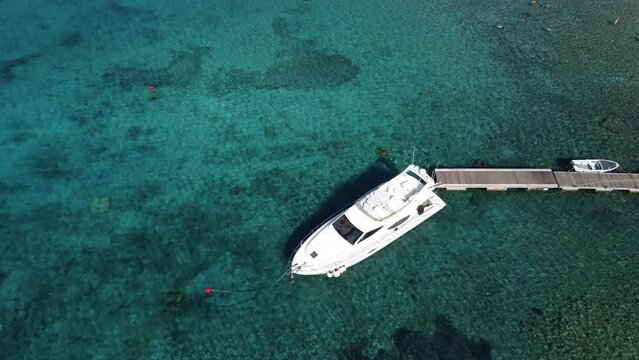 People swimming in crystal clear water of Blue Lagoon in Veliki Budikovac with a Ferretti Yacht moored to wooden Jetty. Aerial