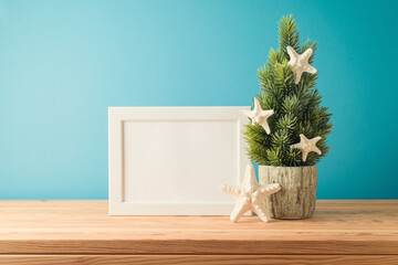Christmas in July concept with Christmas tree, frame mock up and  starfish on wooden table over blue background