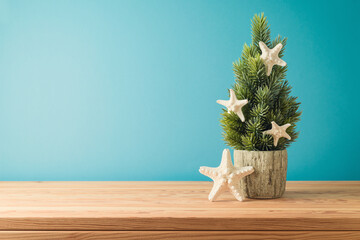 Christmas in July concept with Christmas tree and  starfish on wooden table over blue background