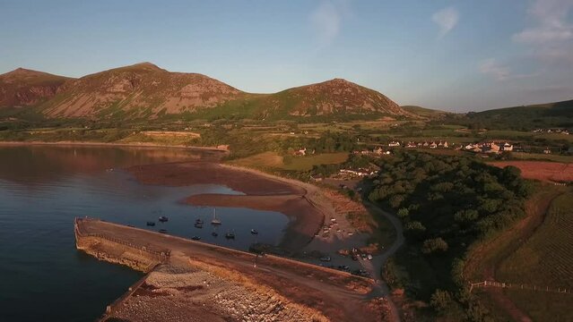Descending aerial view of Trefor bay with backdrop of snowdonia mountains with blue skies on a summers day across the Irish Sea on the Llyn Peninsula in North Wales