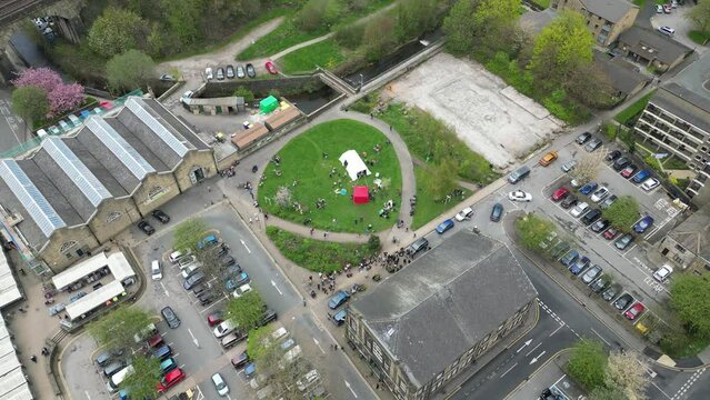 Sweeping drone shot of todmorden town centre markets and carpark , with a community garden right next door , lovely old buildings and a bustling scene 