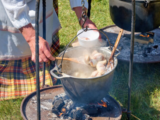 Preparing food in hanging black pot over open fire at historical festival - close up view. Outdoor cooking, hiking, tourism, travelling, camping concept. - Powered by Adobe