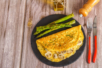 mushroom omelette with wild asparagus on a slate, with cutlery, pepper and extra virgin olive oil