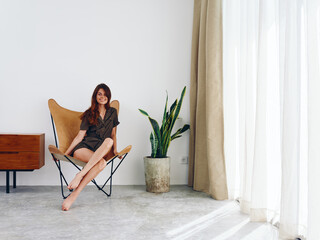 Woman sitting on a chair near the window smiling, modern stylish interior Scandinavian lifestyle,...
