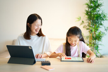 Obraz premium タブレットPCを使って仕事をする女性と遊ぶ女の子