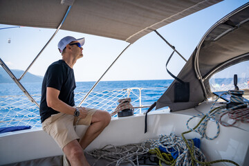 Young man captain controls a sailboat during a journey by sea