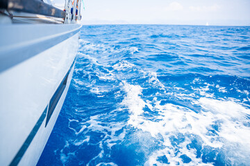 Yacht sailing in an open sea. Close-up view of side of the boat. Clear sky after the rain, waves and water splashes