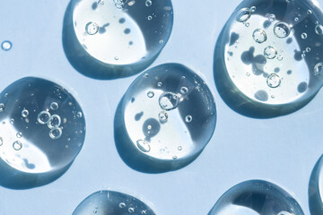 Drops of transparent liquid serum macro blue background. Cosmetic background with toner texture.