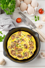 Omelette with mushrooms and herbs in a pan on a white wooden background. Healthy breakfast. Top view. Copy space.