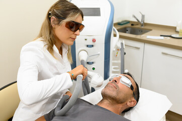 Obraz premium Professional cosmetologist treating patient with laser on bed in clinic