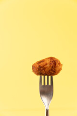 Homemade traditional spanish croquette on a fork on yellow background isolated
