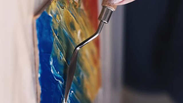 Vertical video. Painting school. Artwork creation. Female artist. Unrecognizable woman creating abstract picture on board canvas with spatula colorful paints.
