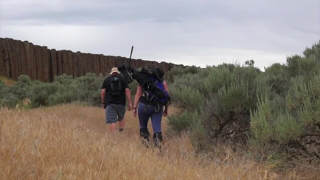 Hikers with big camera on tripod hike in sagebrush to rock columns
