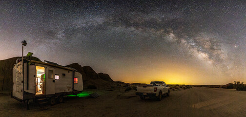 Travel trailer and pickup truck in a remote location in Anza-Borrego Desert State Park. Milky Way galaxy and stars shine in the sky above.