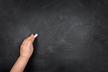 Left-handed child writing with chalk on empty school blackboard, copy space