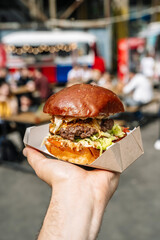 Street food burger on hand on hipster food market background. Grill and barbecue food