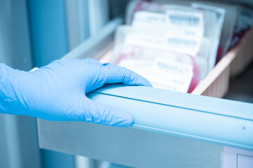 Close up scientist hand holding red blood bag in storage refrigerator at blood bank unit...