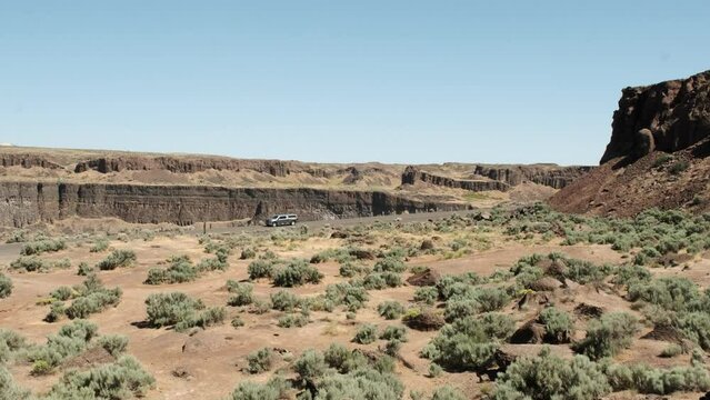 Truck drives on road past Frenchman Coulee cliffs against blue sky