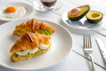 Croissant sandwich with egg,avocado on white dish and honey, coffee. breakfast and healthy food...