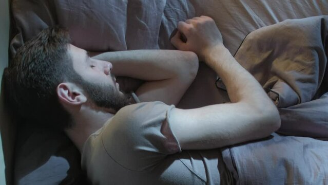 Vertical video. Trouble sleeping. Night insomnia. Rest problem. Anxious man tossing turning alone late in bed in dark home bedroom.