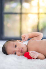 A very young Asian baby is lying on a white bed and the baby looks around. - 615692576