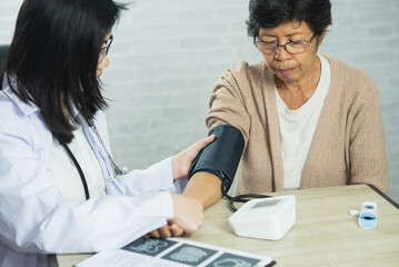 Woman doctor measuring blood pressure for elderly female patient on the doctor's office desk....