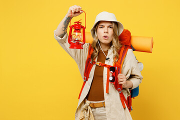 Young woman carry backpack with stuff mat hold in hand lantern look camera isolated on plain yellow background. Tourist leads active lifestyle walk on spare time. Hiking trek rest travel trip concept.