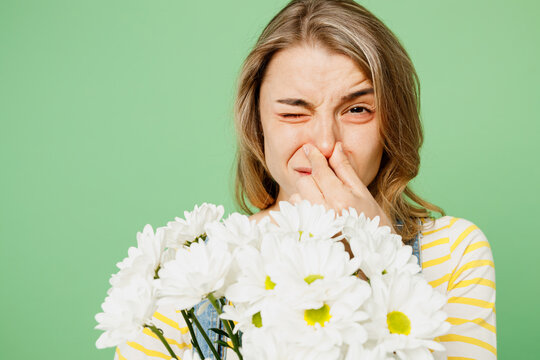 Close up sick unhealthy ill allergic sad woman has red watery eyes close runny stuffy sore nose suffer from allergy trigger symptom fever hold bouquet fowers isolated on plain green background studio
